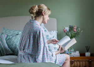 Woman sitting on her bed wearing Doc Cotton sleepwear with a colorful design