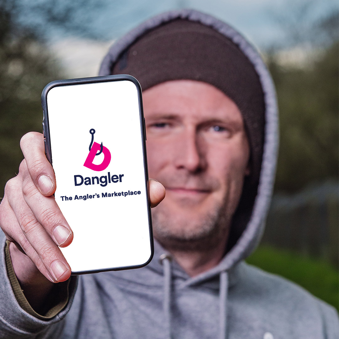 A man holding a mobile with "Dangle The Angler's Marketplace" on the screen