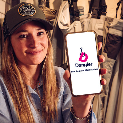 A woman holding a mobile with "Dangle The Angler's Marketplace" on the screen
